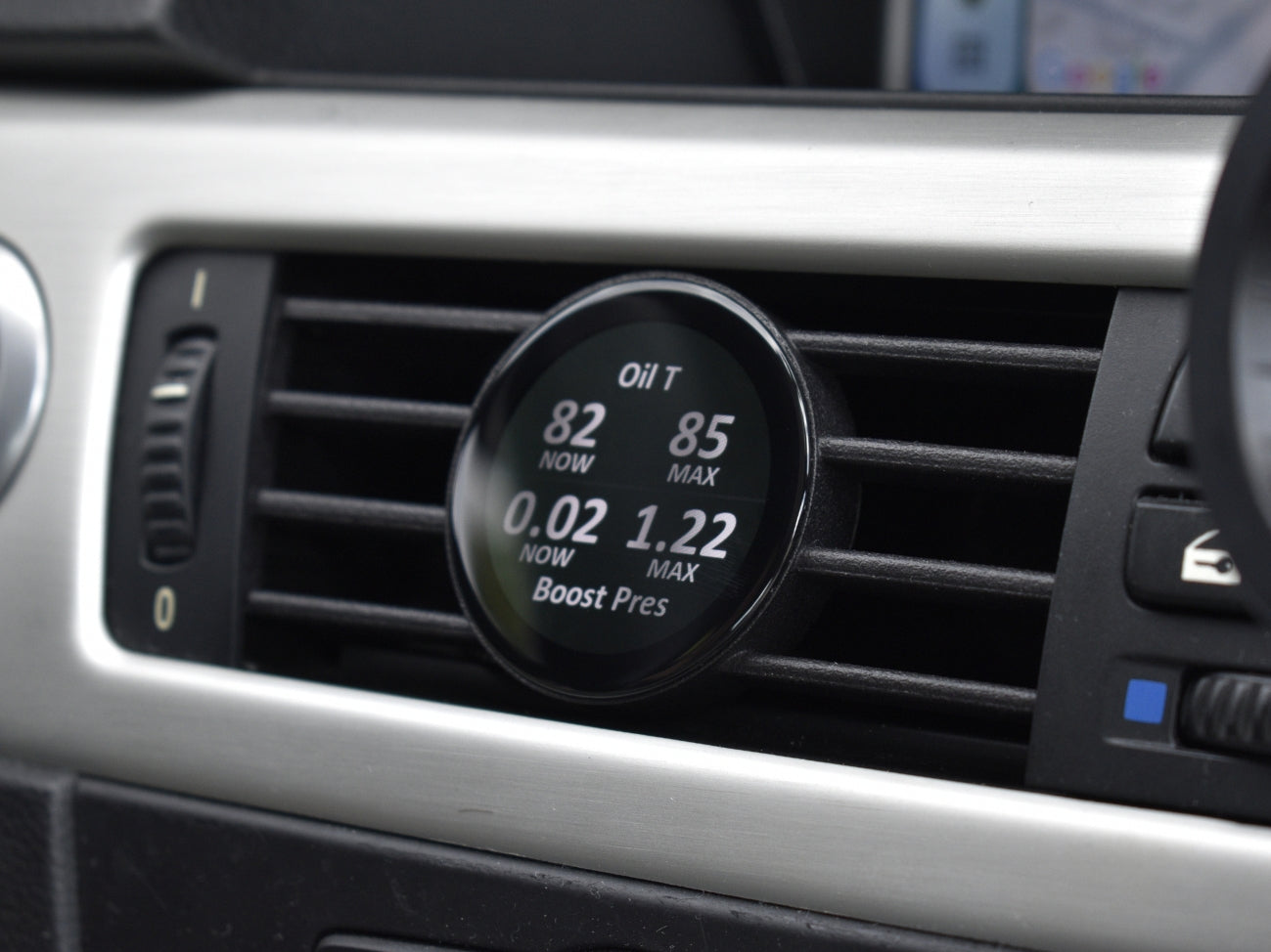 Ein guter Alt-Text für dieses Bild wäre:
"Ein COREDISPLAY Datendisplay, das in einen Lüftungsschlitz eingebaut ist. Der Bildschirm zeigt die aktuelle und maximale Öltemperatur sowie den aktuellen und maximalen Ladedruck an.