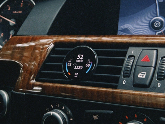 Ein COREDISPLAY Datendisplay, eingebaut in den Lüftungsschlitz eines BMW mit Holzdekor-Armaturenbrett. Das Display zeigt die aktuelle Geschwindigkeit von 51 km/h und andere Fahrzeugdaten an.