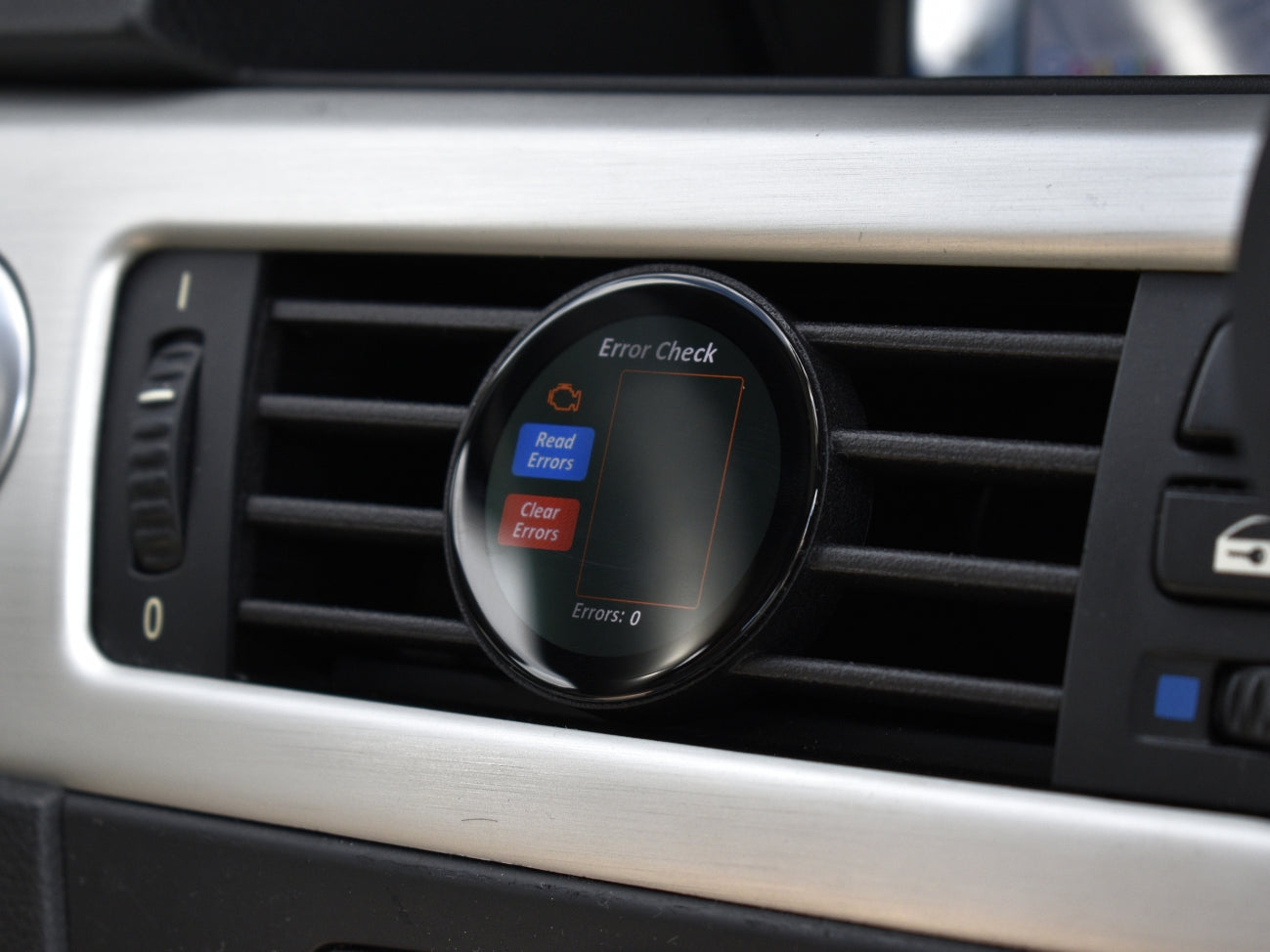 Ein COREDISPLAY Datendisplay in einem Lüftungsschlitz, das den 'Error Check' Modus anzeigt. Der Bildschirm ist leer und meldet 'Errors: 0', was darauf hinweist, dass keine Motorsteuergeräte-Fehler gefunden wurden.