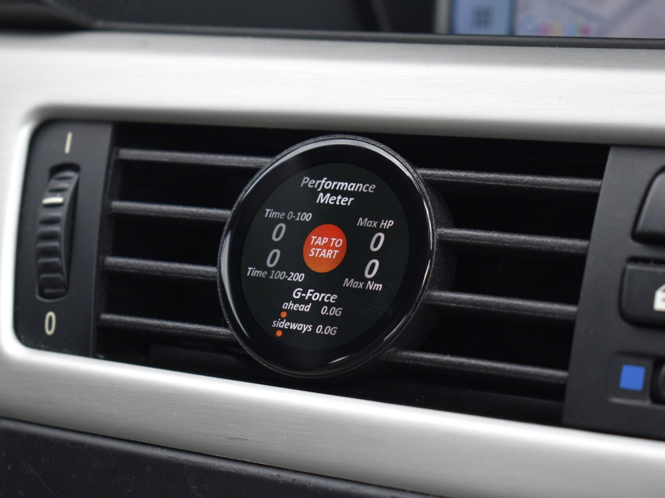 Ein COREDISPLAY Datendisplay in einem Lüftungsschlitz, das den 'Performance Meter' Modus anzeigt. Das Display misst Beschleunigungszeiten von 0-100 km/h und 100-200 km/h sowie G-Kräfte, maximale PS und Drehmoment.