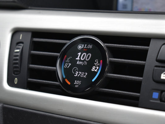 Ein COREDISPLAY GEN3 Datendisplay, eingebaut in den Lüftungsschlitz eines BMW 3er (E9x). Das Display zeigt aktuelle Leistungsdaten wie Geschwindigkeit (100 km/h), Ladedruck (1.06 bar), Kühlmitteltemperatur und die aktuelle PS-Zahl an.