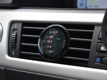 Ein COREDISPLAY Datendisplay, eingebaut in einen Lüftungsschlitz im Auto. Das Display zeigt verschiedene Leistungsdaten an, darunter Ladedruck, Luftmassenstrom in kg/h, G-Kräfte, Drehzahl (RPM) und Batteriespannung.